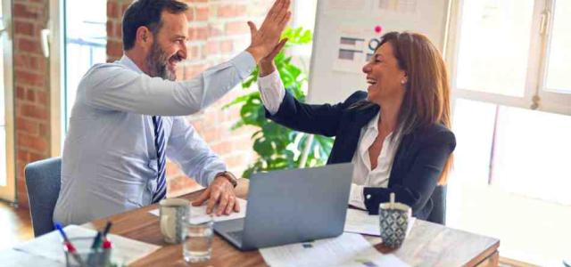 Two people at work high fiving at a desk